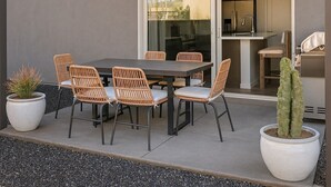 Een terras buiten met een tafel, stoelen, een potplant en een schuifdeur naar een keuken.