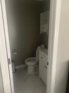 Ein kleines, schwach beleuchtetes Badezimmer mit Toilette, einem kleinen Mülleimer und einem Schrank mit Spiegel.