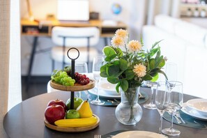 Ett matbord med en fruktskål, en vas med blommor och tomma vinglas.