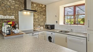 Una cocina con pared de piedra, lavadora integrada, microondas y ventana con vista a árboles.