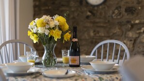 Una mesa de comedor con un jarrón de flores, una botella de vino y un vaso de jugo de naranja.