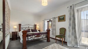 Un dormitorio con cama, mesitas de noche, una silla, una ventana con cortinas y un cuadro en la pared.