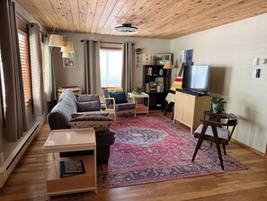 A cozy living room with a sofa, armchair, coffee table, and a TV. - Charming Miller Cabin in McCall! Sauna, utilities, snow removal, pet friendly! (McCall)