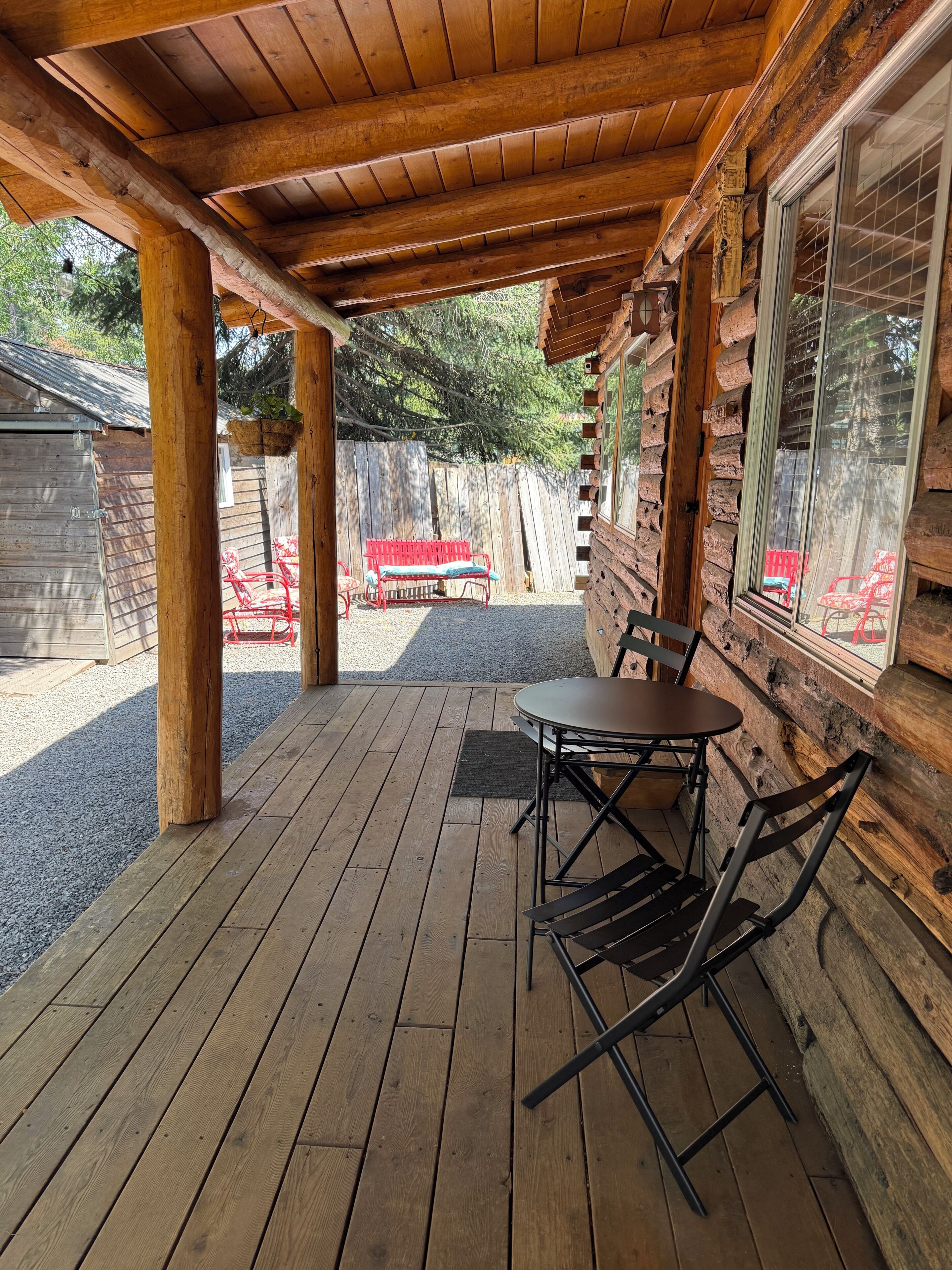 A wooden deck with a table and chairs, a red bench, and a wooden cabin with a window.