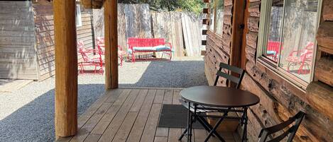 A wooden deck with a table and chairs, a red bench, and a wooden cabin with a window.