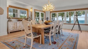 Uma sala de jantar com uma mesa de madeira, cadeiras brancas e um candelabro.