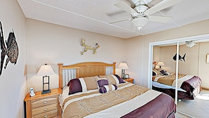 Une chambre à coucher comprenant un lit, des tables de chevet, un ventilateur de plafond, des œuvres d’art murales et un miroir.