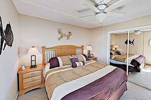 Ein Schlafzimmer mit Bett, Nachttischen, Deckenventilator, Wandbildern und einem Spiegel.
