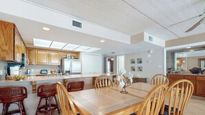 Une cuisine spacieuse dotée de meubles en bois, d’un grand îlot central avec des tabourets et d’un coin repas comprenant une table et des chaises en bois.
