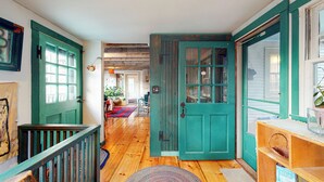 Un pasillo con piso de madera, puertas verde azulado, una escalera y vistas a otra habitación.