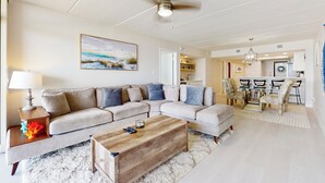 Ein Wohnzimmer mit einem Ecksofa, einem Holztisch und einem Deckenventilator.