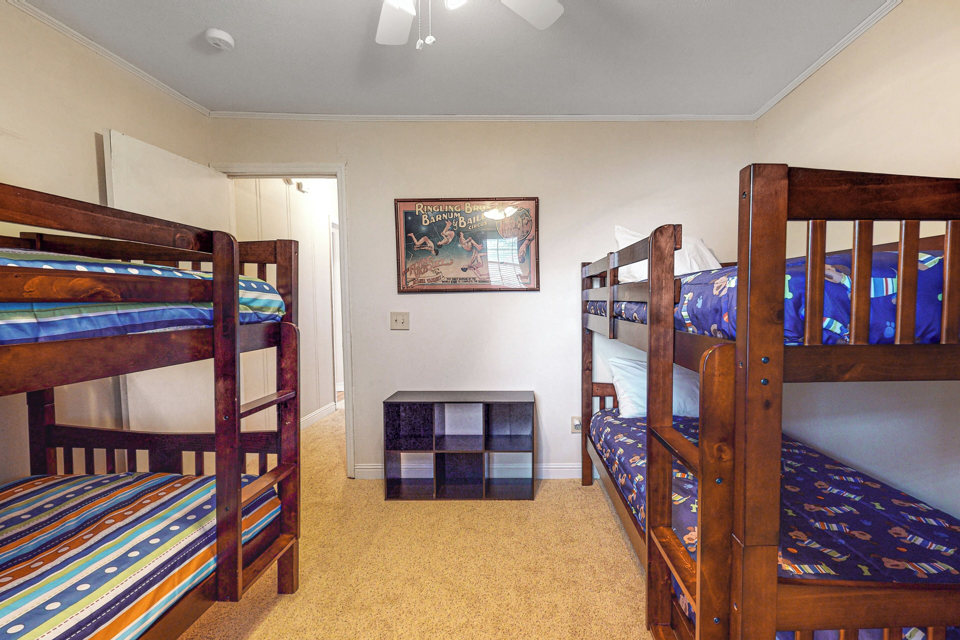 Una habitación con literas, ventilador de techo, un cuadro enmarcado en la pared y un pequeño armario.