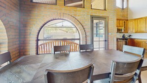 Un comedor con una gran mesa de madera y sillas, un muro de ladrillo y vistas a un balcón exterior a través de un arco.