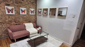Een woonkamer met een bakstenen muur, een roze bank, een glazen salontafel en een witte vloerkleed.