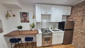 Een moderne keuken met witte kasten, een gasfornuis, een roestvrijstalen koelkast en een bakstenen muur.