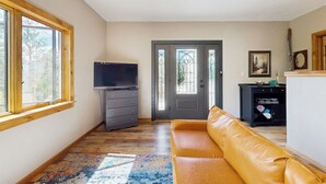 Ein Zimmer mit Holzboden, einem braunen Ledersofa, einem Fernseher auf einer Kommode und einer Tür mit Buntglasfenstern.
