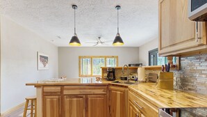 Eine Küche mit Holzschränken, einer großen Kochinsel, Edelstahlgeräten und Pendelleuchten.