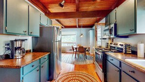 Una cocina con armarios color turquesa, techo de madera, cafetera y comedor con sillas.