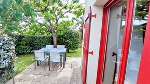 A patio with a table and chairs, a tree, and a red door. - Maisonnette 4 personnes proche de la plage - WIFI (SARZEAU)