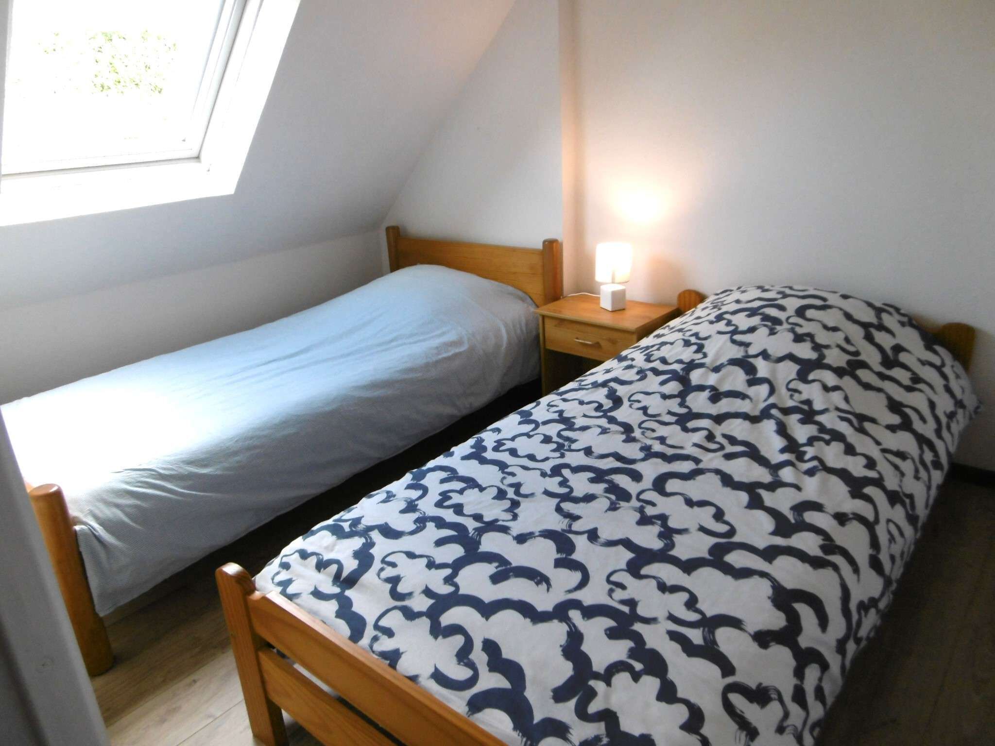 A small room with two single beds, a nightstand with a lamp, and a window.