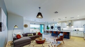 A modern living room with a sectional sofa, a coffee table, and a dining area with a bar. - Mtn-View Patio & Resort Perks: Verde River Retreat (Rio Verde)
