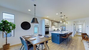 A modern kitchen with a central island, white cabinetry, and a dining area with a wooden table and chairs. - Mtn-View Patio & Resort Perks: Verde River Retreat (Rio Verde)