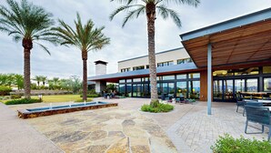 A modern building with a covered outdoor seating area, stone patio, and palm trees. - Mtn-View Patio & Resort Perks: Verde River Retreat (Rio Verde)