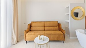 Ein modernes Badezimmer mit einem beigen Sofa, einem runden Spiegel und einer weißen Badewanne.