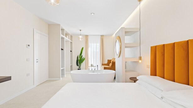 Ein modernes Hotelzimmer mit einem großen Bett, einer Badewanne, einem Schminktisch mit Spiegel und einer Pflanze.