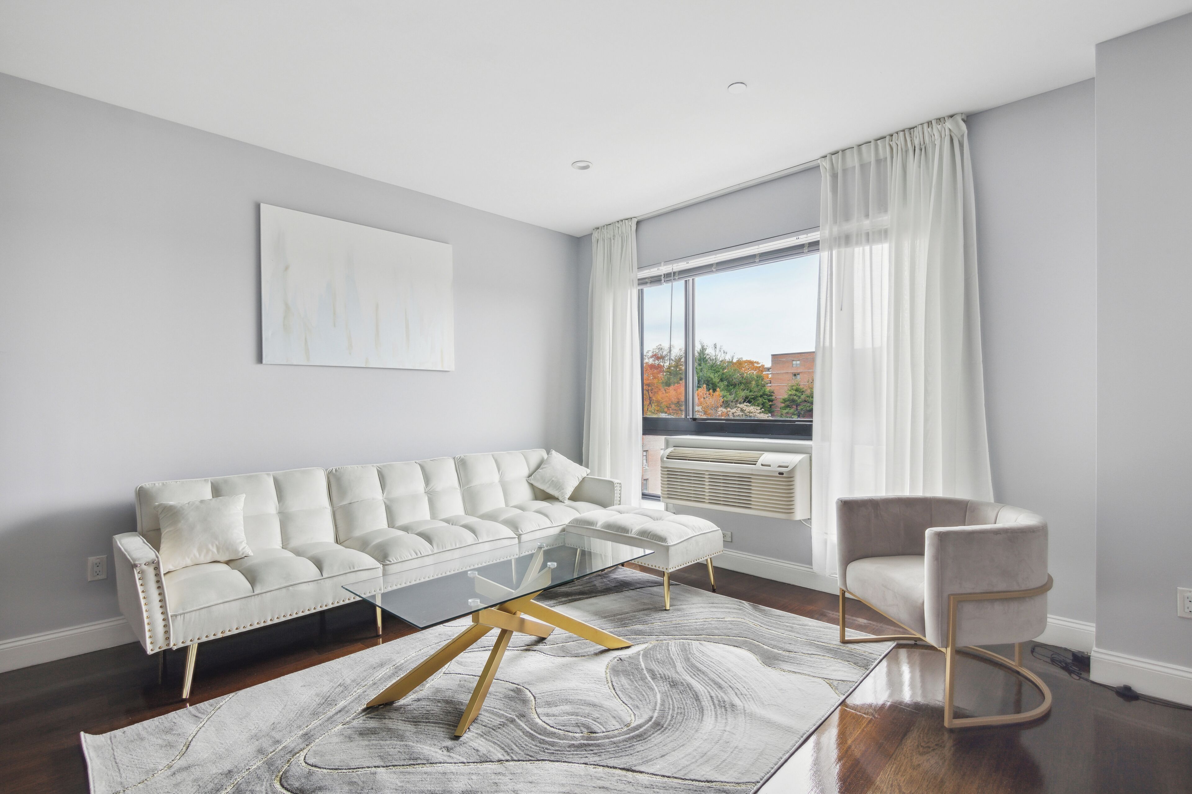 Uma sala de estar moderna com um sofá branco, uma mesa de centro de vidro e uma poltrona bege.
