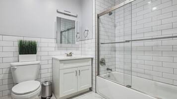 Un baño moderno con inodoro, lavamanos, tocador y ducha con mampara de vidrio.