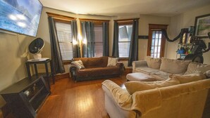 Ein Wohnzimmer mit braunem Sofa, einem beigefarbenen Sofa, einem Holztisch und einem flachbildfernseher, der an der Wand montiert ist.