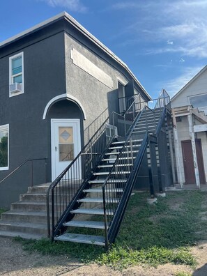 A two-story building with a black exterior, a white door, and a metal staircase leading to the second floor.