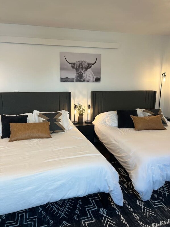 A hotel room with two beds, a large wall-mounted artwork of a bull, and a floor lamp.