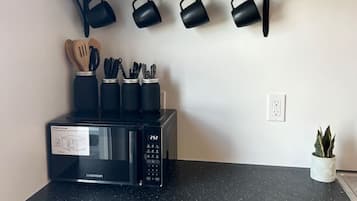 A kitchen with a black countertop, a microwave, a shelf with black kitchenware, and a potted plant.