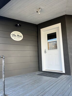A grey exterior wall with a white door and a sign that reads 'Ole Mae Apartments.'