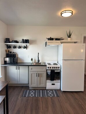 A compact kitchen with white cabinets, a white refrigerator, a stove, and a microwave. There is a black countertop and a patterned rug on the floor.