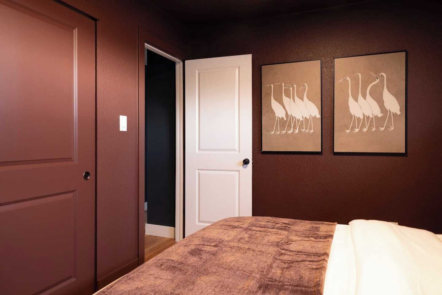 Un dormitorio con una cama, una puerta y dos cuadros de aves colgados en la pared.