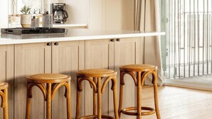 Una cocina con encimera blanca, taburetes de madera, una lámpara colgante y vistas al exterior.