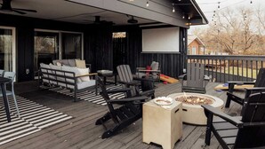 Una terraza techada al aire libre con una chimenea, una zona de estar y una gran pantalla para ver desde fuera.