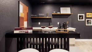Zona de bar con mostrador negro, estantes con vasos, un cuadro enmarcado y un libro titulado 'SCRABBLE'.