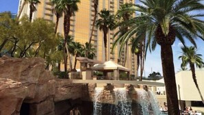 A high-rise hotel with a pool area featuring palm trees and a waterfall. - MGM Signature - Strip view suite (Las Vegas)