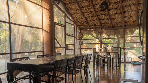 A dining area with a large table and chairs, large windows, and a thatched roof. - La Aldea Cabañas y Glamping (Isla Holbox)