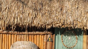 A stone statue of a figure with a headdress, a wooden fence, and a green door with a dreamcatcher. - La Aldea Cabañas y Glamping (Isla Holbox)