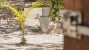 A sandy outdoor area with a palm tree, a stone planter, and a metal chair. - La Aldea Cabañas y Glamping (Isla Holbox)
