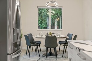 Un espace repas moderne avec une table ronde, six chaises et une grande fenêtre donnant sur un paysage verdoyant.