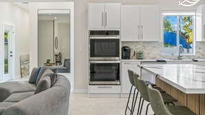 Eine moderne Küche mit weißen Schränken, einem eingebauten Backofen und einer großen Kochinsel mit Barhocker.