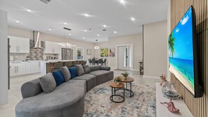 Ein modernes Wohnzimmer mit einem grauen Ecksofa, einem Couchtisch und einem Fernseher, der eine Strandansicht zeigt.