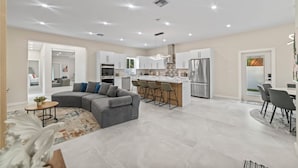 Eine moderne Küche mit Edelstahlgeräten, ein Essbereich mit Bar und ein Wohnzimmer mit grauem Ecksofa.