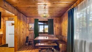 L’intérieur d’un chalet en bois comprend une table à manger, des bancs, un réfrigérateur et une grande fenêtre avec des rideaux.